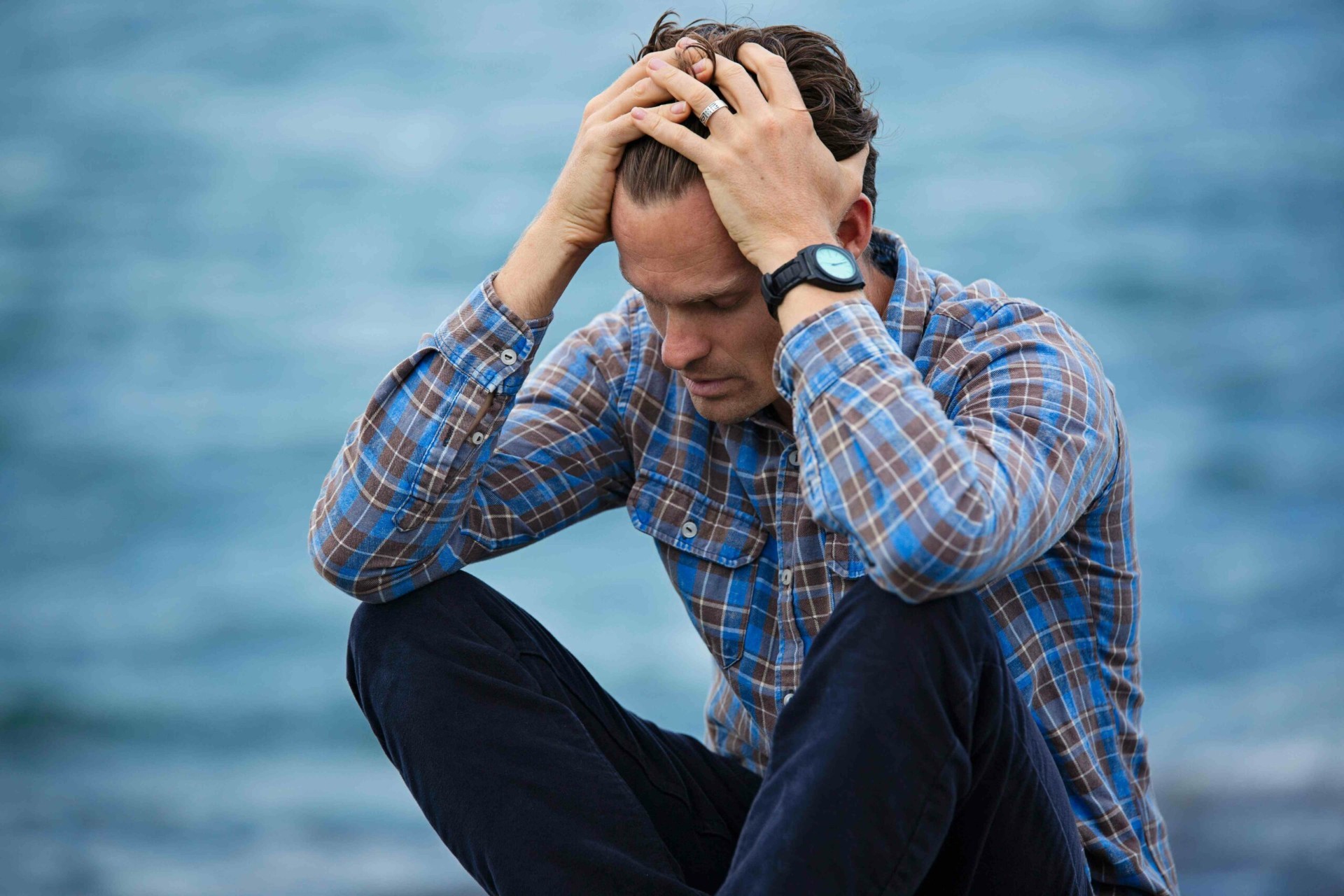 Homme les mains dans la tête au bord de l'eau illustrant le poids du stress et des angoisses au quotidien accompagnés par le neurofeedback dynamique NeurOptimal®